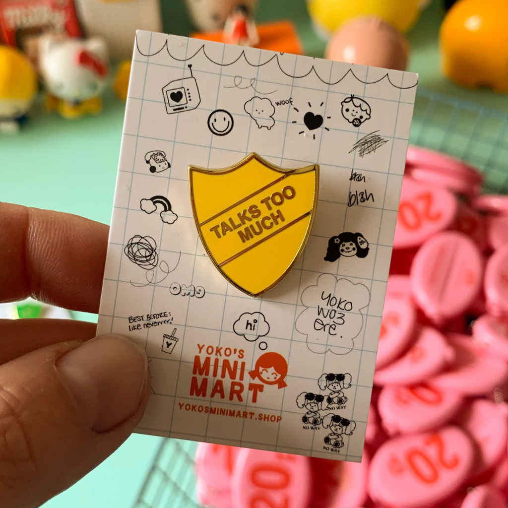 Yellow badge with 'Talks Too Much' text on a card held by a hand, with colorful background